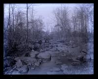 Bed of Naaman's Creek, [Claymont, DE], looking up toward railroad bridge. Mother on a large rock [graphic].