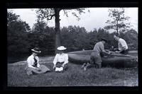 [Two women sit on grass; two men work on canoes], Down Rancocas, [NJ] [graphic].