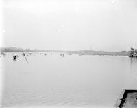 [River scene, with boats, industrial facilities, and a bridge in background] [graphic].