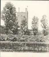 [Scene with fence, garden, and buildings] [graphic].