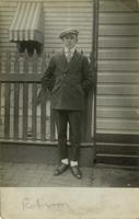 Young man standing beside a wooden fence and house, Philadelphia.