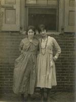 Two young women standing in front of open window of brick house, Philadelphia.