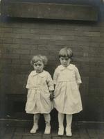 Two little girls standing against a brick wall in their summer dresses, Philadelphia.