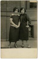 Two nicely dressed young women standing in front of brick building, Philadelphia.