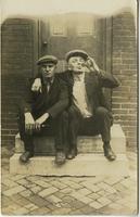 Two workmen sitting on a stoop, one drinking out of a beer bottle, Philadelphia.