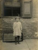 Young girl standing on sidewalk in front of window, Philadelphia.