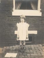 Girl in checked ruffled dress in front of window, Philadelphia.