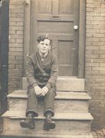 Young man in cardigan sweater sitting on wooden stoop, Philadelphia.