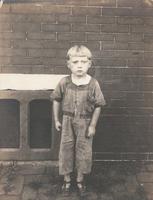 Blond boy in overalls standing on sidewalk, Philadelphia.