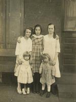 Three teenage girls and two little girls standing in front of brick house, Philadelphia.