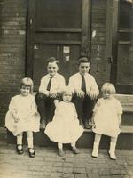 Group of boys and girls sitting on wooden stoop in front of screen doors, Philadelphia.