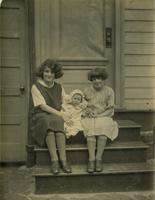 Two girls with an infant sitting on wooden steps of wooden house, Philadelphia.