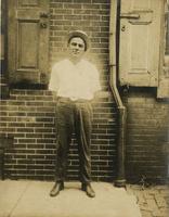 Man in straw bowler standing in front of brick house, Philadelphia.