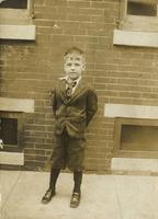 Little boy in suit standing in front of a brick house, Philadelphia.