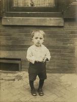 Little boy, possibly with rickets, standing in front of brick house, Philadelphia.