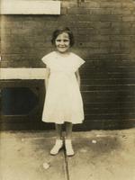 Little girl in white dress standing outside a brick house, Philadelphia.