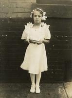 Girl in First Communion dress standing in front of painted brick wall, Philadelphia.