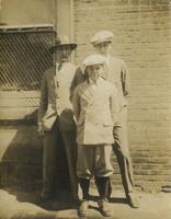 Boy and two young men in suits standing outside brick building, Philadelphia.