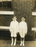 Two little boys dressed for First Communion standing in front of a brick house, Philadelphia.