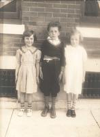 Two girls and a boy standing in front of brick house, Philadelphia.