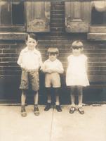 Three children in front of a brick wall with two windows, Philadelphia.