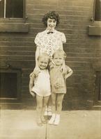 Teenage girl standing with two little girls in front of brick house, Philadelphia.