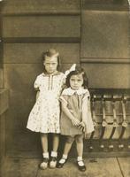 Two little girls standing in front of a stone building, Philadelphia.