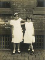 Two girls standing in front of brick wall with their arms around one another, Philadelphia.