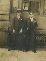 Two young men in three-piece suits standing in front of brick and brownstone house, Philadelphia.