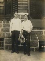 Two young men with caps in their hands standing in front of stone porch, Philadelphia.