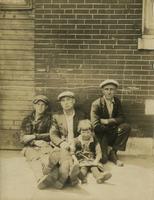 Three men and a little girl sitting on the sidewalk in front of a brick house, Philadelphia.