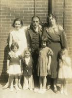 Three adults and four small children standing in front of brick wall, Philadelphia.