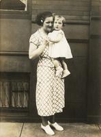 Woman holding child standing outside a brick and brownstone house, Philadelphia.