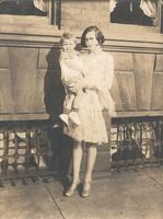 Young woman standing outside a brick and stone house holding a child, Philadelphia.