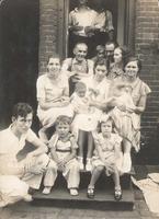 Group of fourteen people sitting and standing in the doorway of a brick house, Philadelphia.