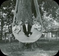[Four children in a swing suspended from a tree.]