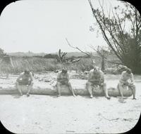 [Group sitting on a log on a beach.]