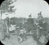 [Outing in the country, group sitting on fence eating lunch.]