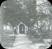 [Stone church, arched entranceway from dirt path.]