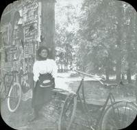 [Catharine Rupp Doering sitting on stone wall near covered bridge in a wooded area.]