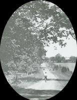 [Woman bicycling along a dirt road in the countryside.]