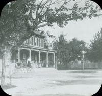 [Woman standing on steps near open porch of dwelling.]