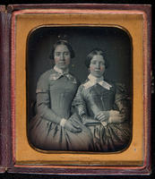 [Portrait of two unidentified, young women seated wearing close fitting long sleeved dresses with crossed collars.]
