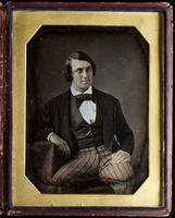 [Seated portrait of an unidentified young man wearing striped trousers, with his right hand resting on a low table.]