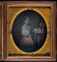[Julianna Wood, aged 5 years, holding a doll in her right hand and pointing to a page in an open album on a table next to her.]